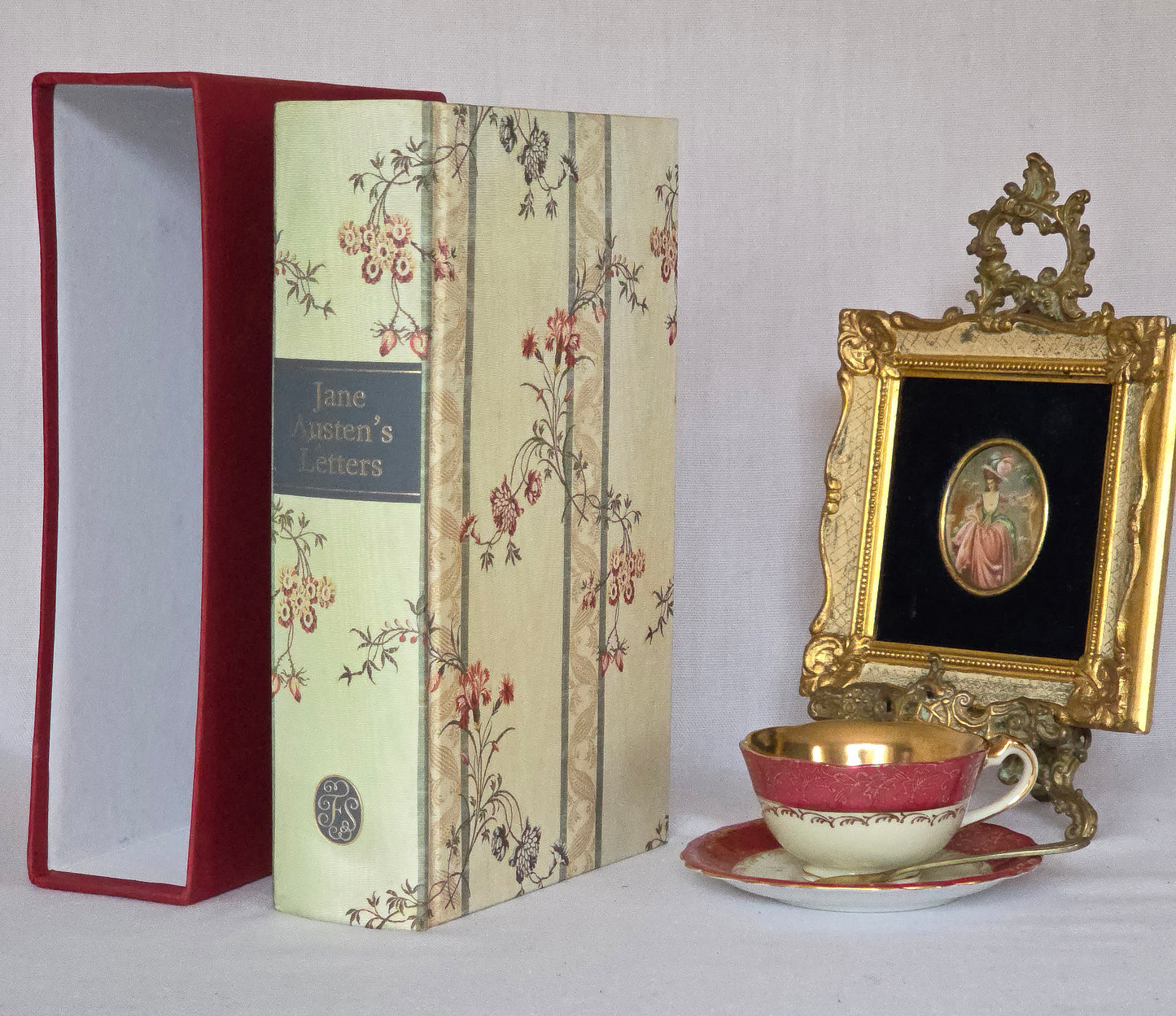 Decorative book being a copy of Jane Austen's Letters, The Folio Society a teacup and saucer, and an ornate gold frame on a white background.