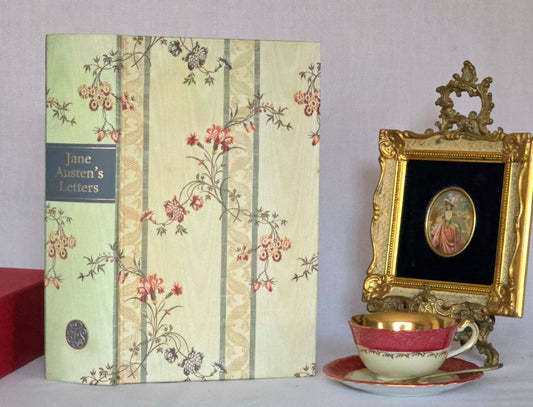 Book titled 'Jane Austen's Letters' with decorative cover, teacup, and ornate frame on a plain background