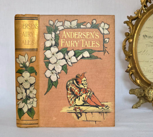 Antique book in light brown cloth, floral decoration, jester and gilt titles saying Andersen's Fairy Tales.