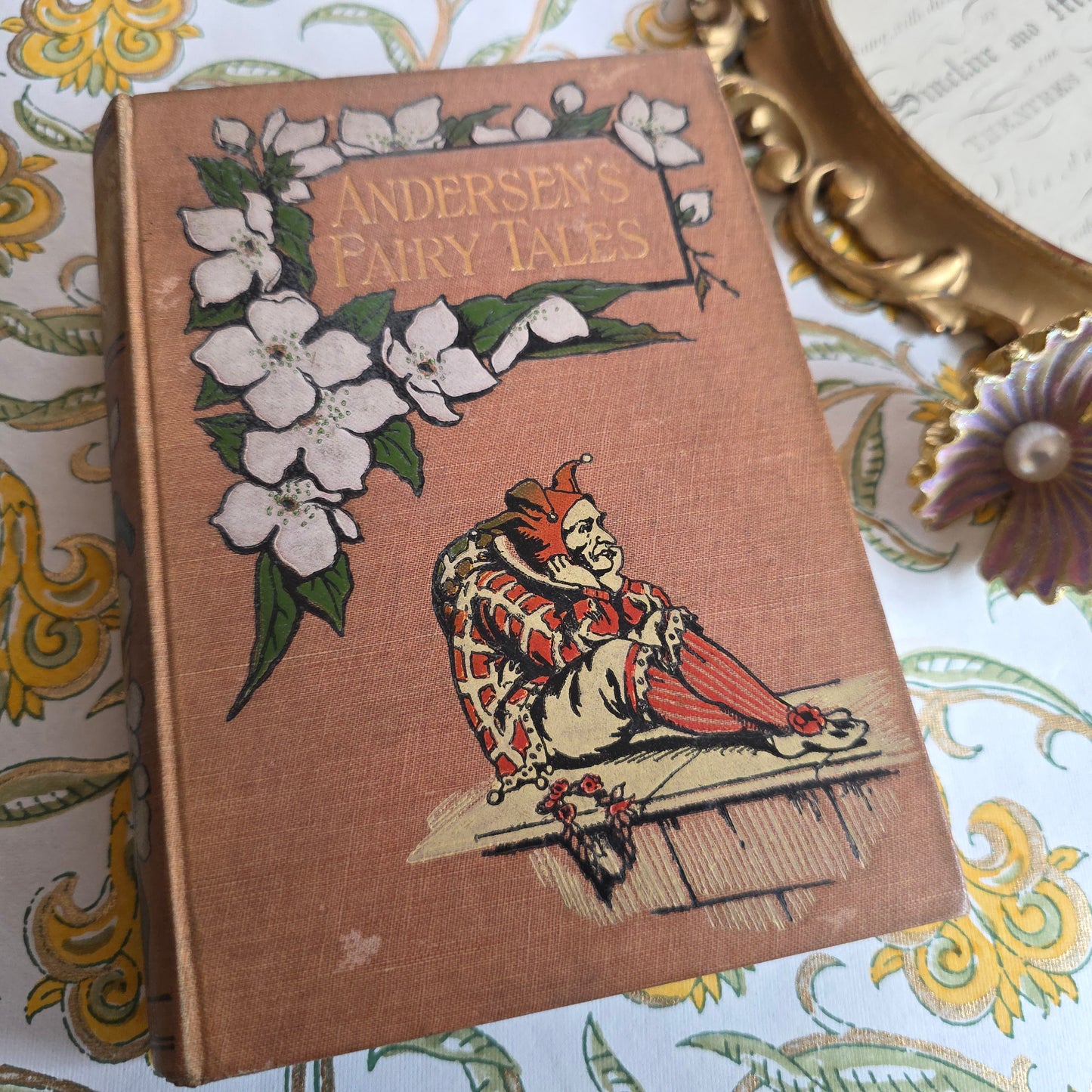 Antique book in light brown cloth, floral decoration, jester and gilt titles saying Andersen's Fairy Tales.