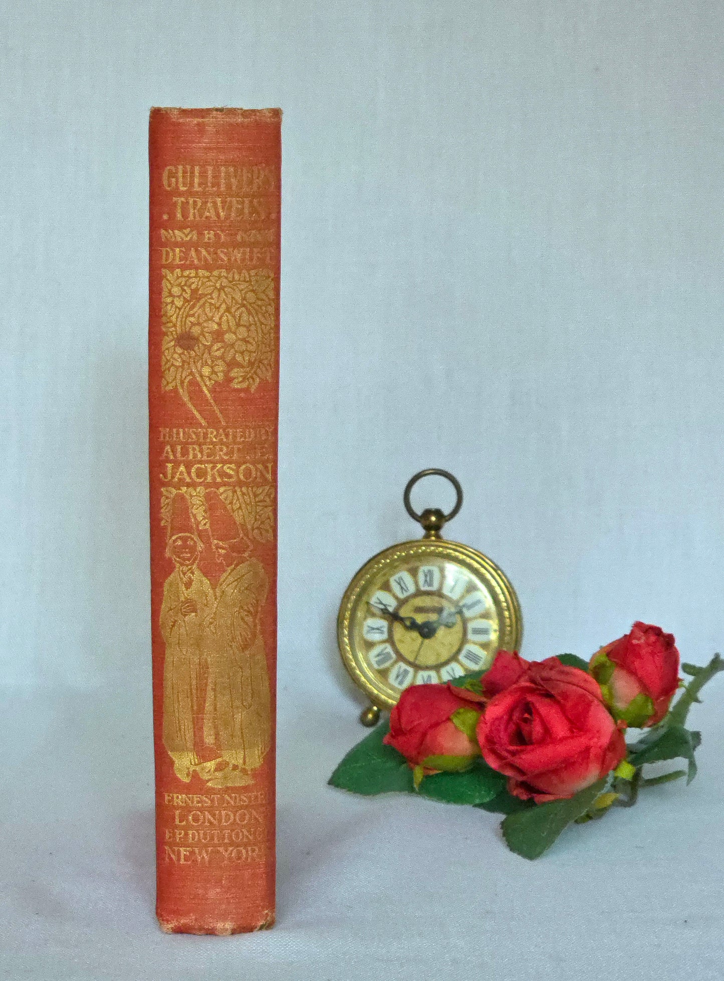 Red book spine titled 'Gulliver's Travels' with gold illustrations on a light gray background. Illustrated by AE Jackson and published by Nister.