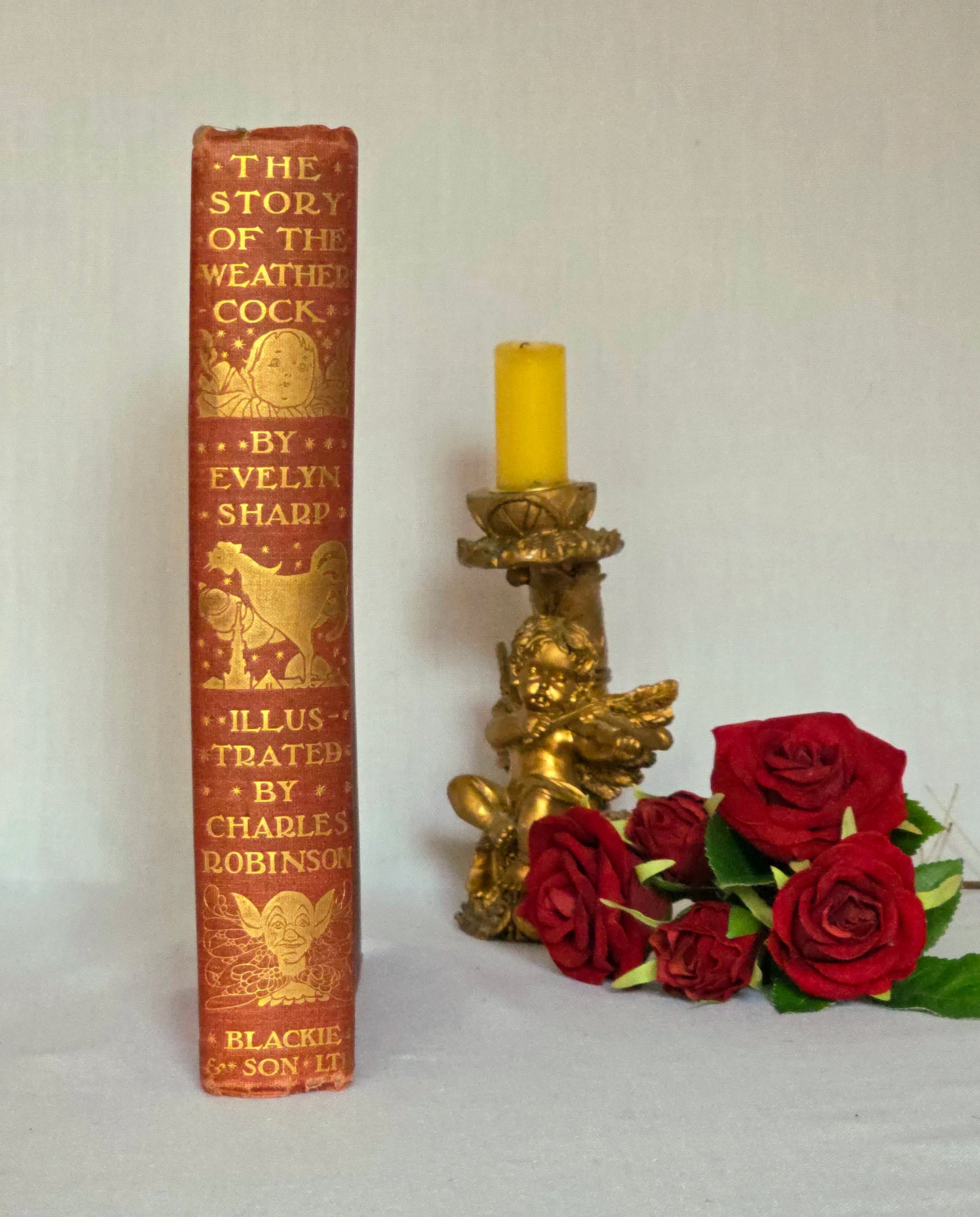 Antique book spine in red cloth with gilt titles saying 'The Story of the Weathercock' by Evelyn Sharp