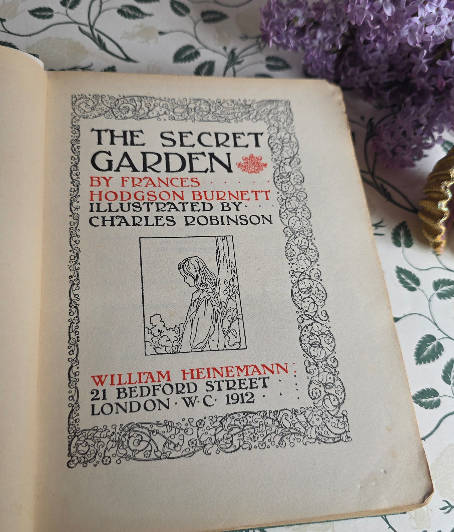Antique book open at title page of 'The Secret Garden' with decorative elements on a floral background.
