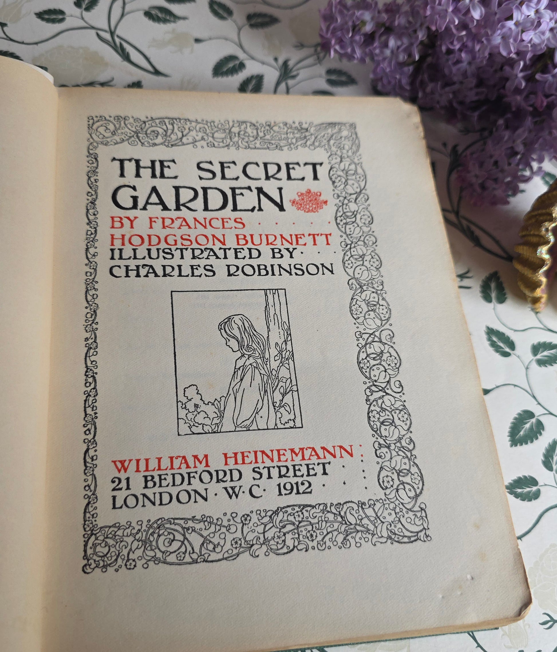 Antique book open at title page of 'The Secret Garden' with decorative elements on a floral background.