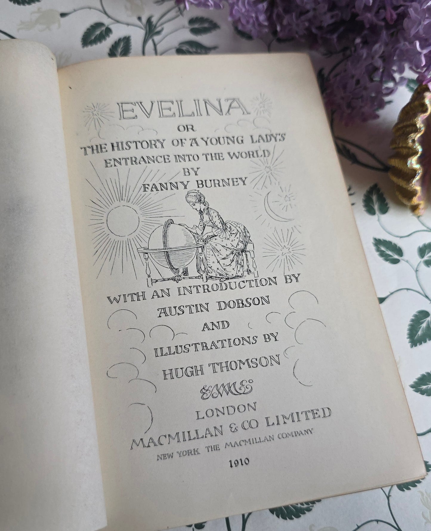 Open antique book titled 'Evelina' showing title page and frontispiece with illustrations on a floral-patterned surface