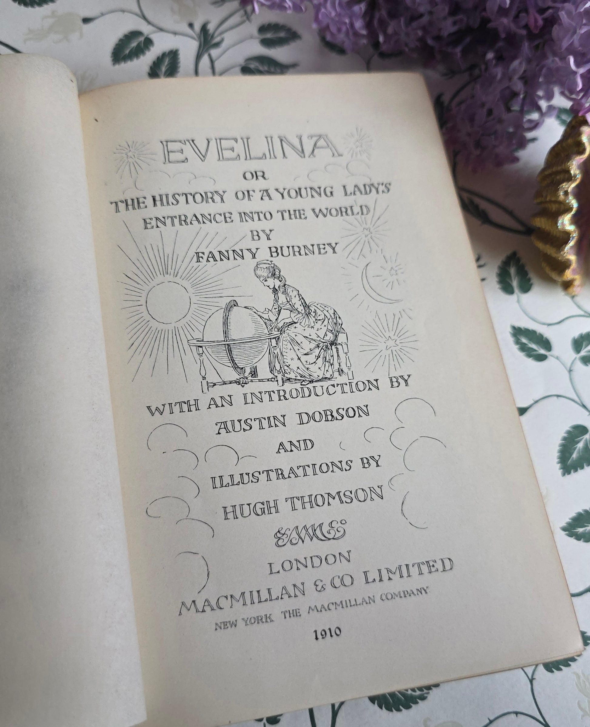 Open antique book titled 'Evelina' showing title page and frontispiece with illustrations on a floral-patterned surface