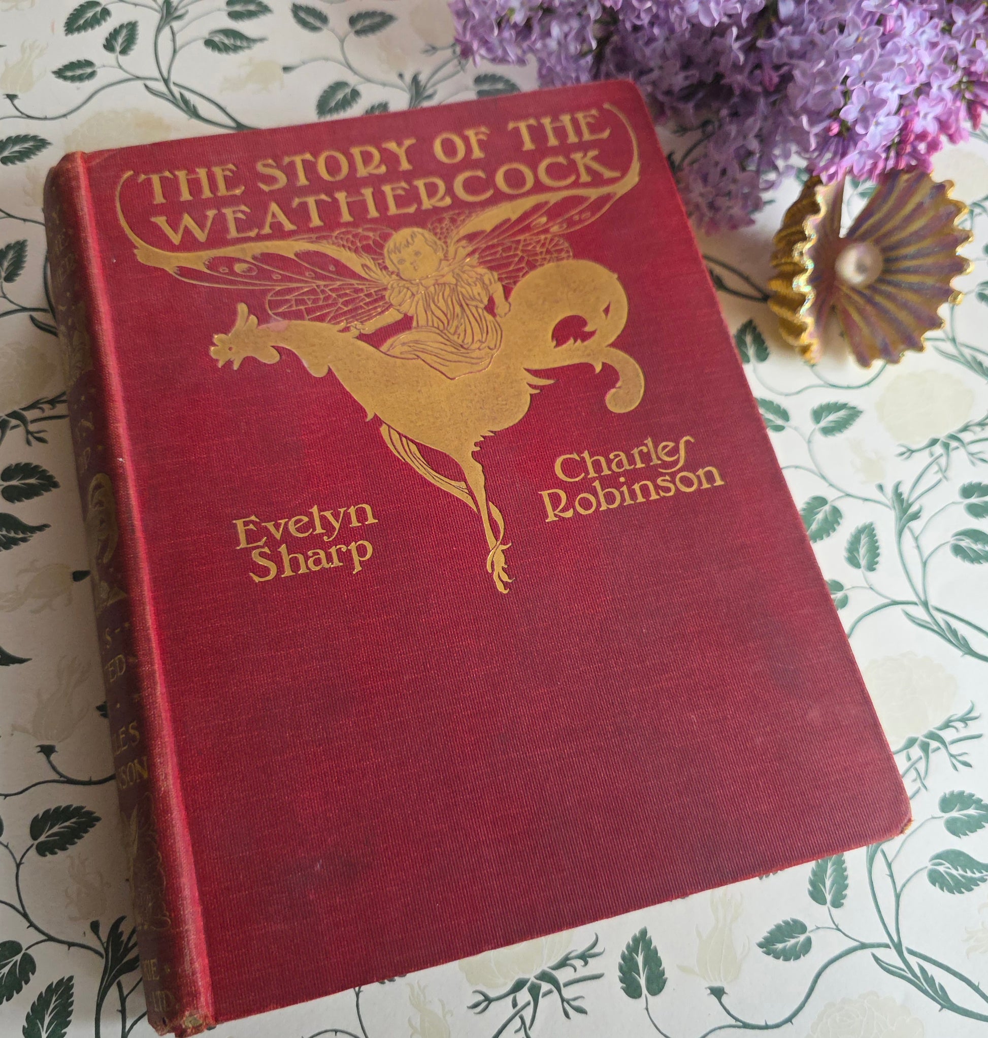 Antique book in red cloth with gilt titles saying 'The Story of the Weathercock' by Evelyn Sharp