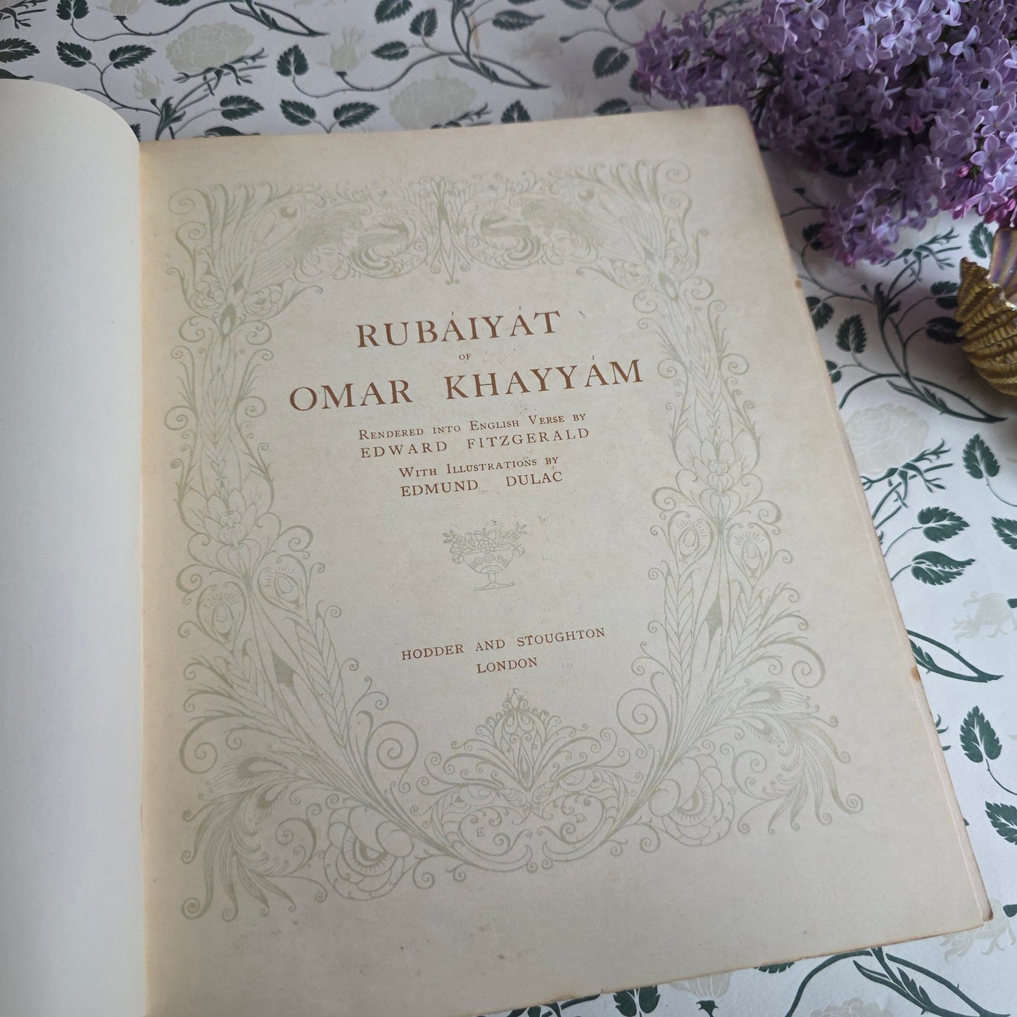 Open book titled 'Rubaiyat of Omar Khayyam' illustrated by Edmund Dulac, with decorative cover on a floral-patterned surface.