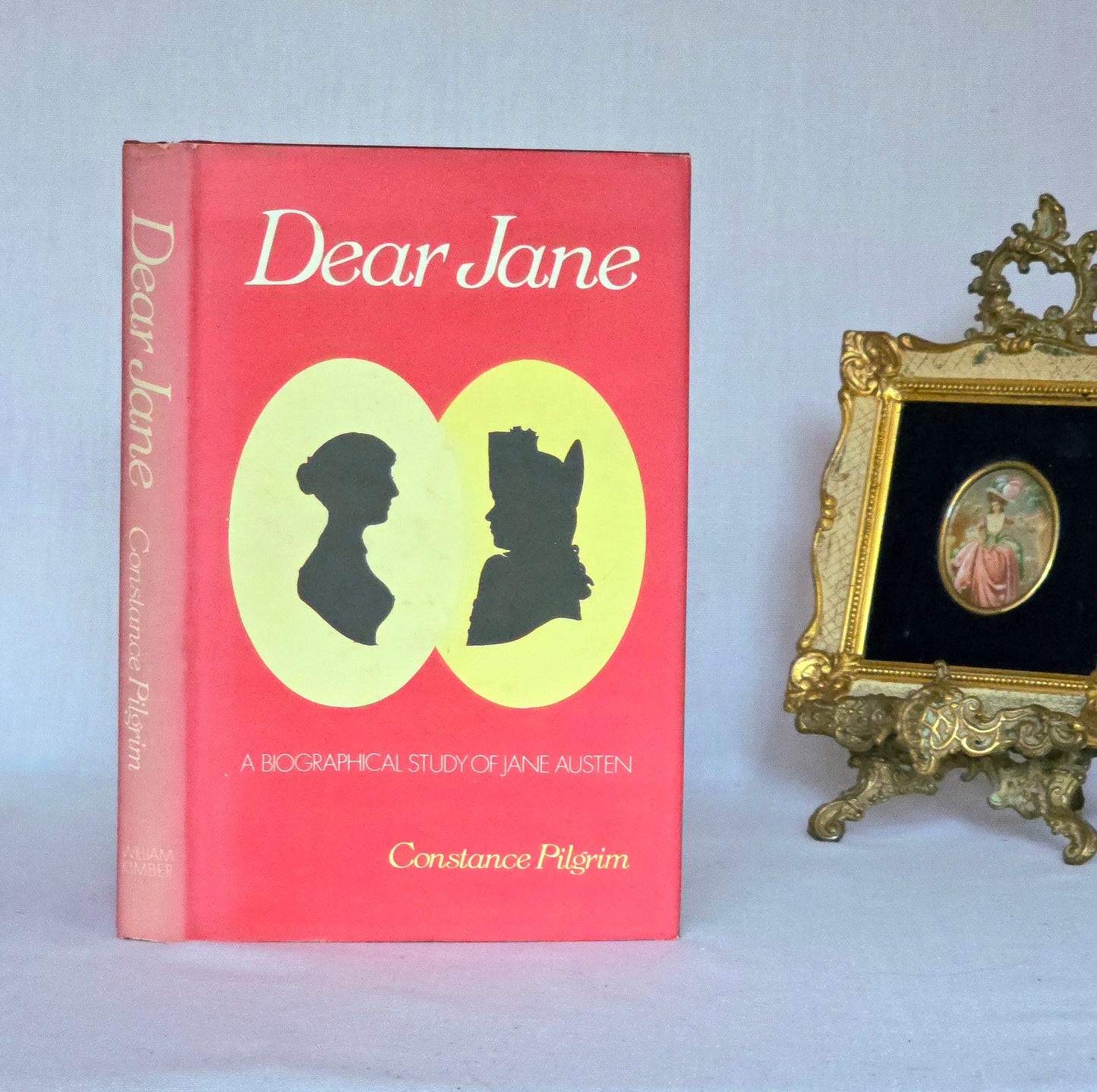 Book titled 'Dear Jane' by Constance Pilgrim with silhouettes on a pink cover, next to a decorative frame.