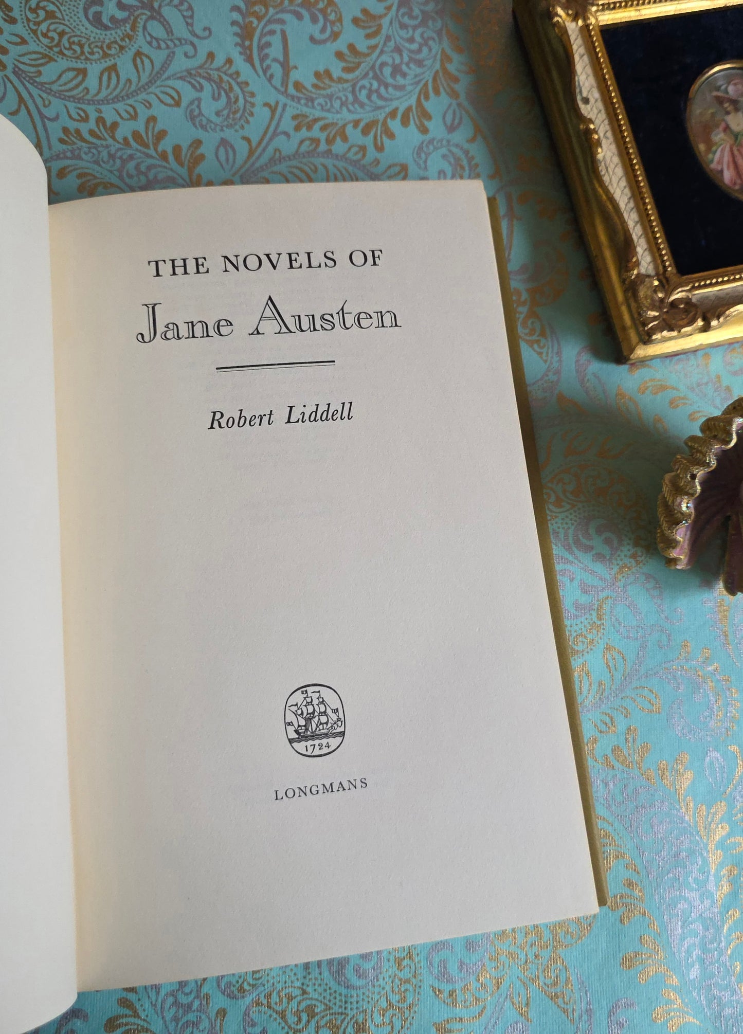 Book titled 'The Novels of Jane Austen' by Robert Liddell on a decorative surface with a gold frame and decorative object.