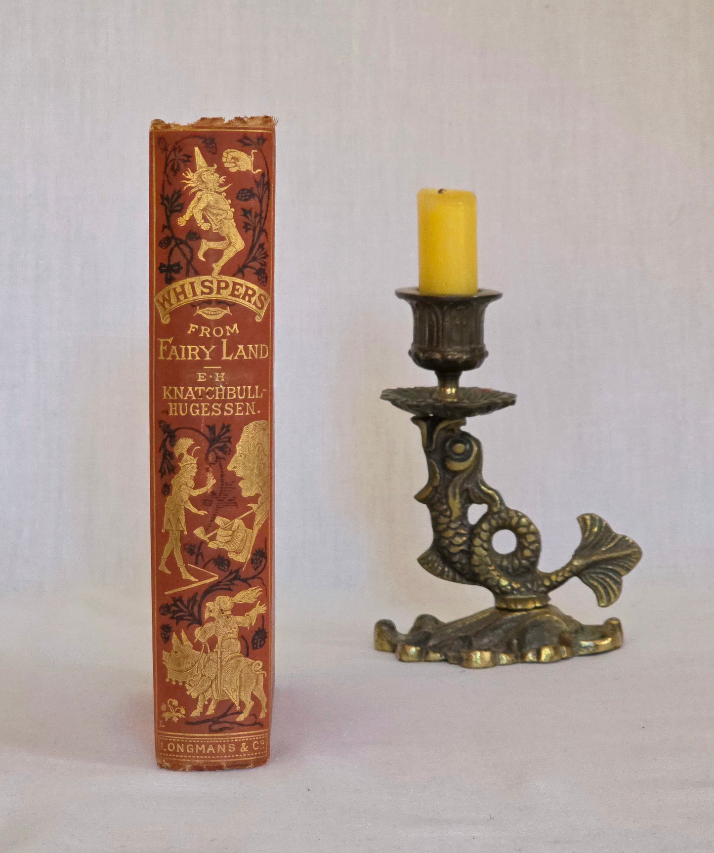 Antique book spine in red cloth with black and gold decoration saying 'Whispers in Fairyland' by Knatchbull-Hugesson