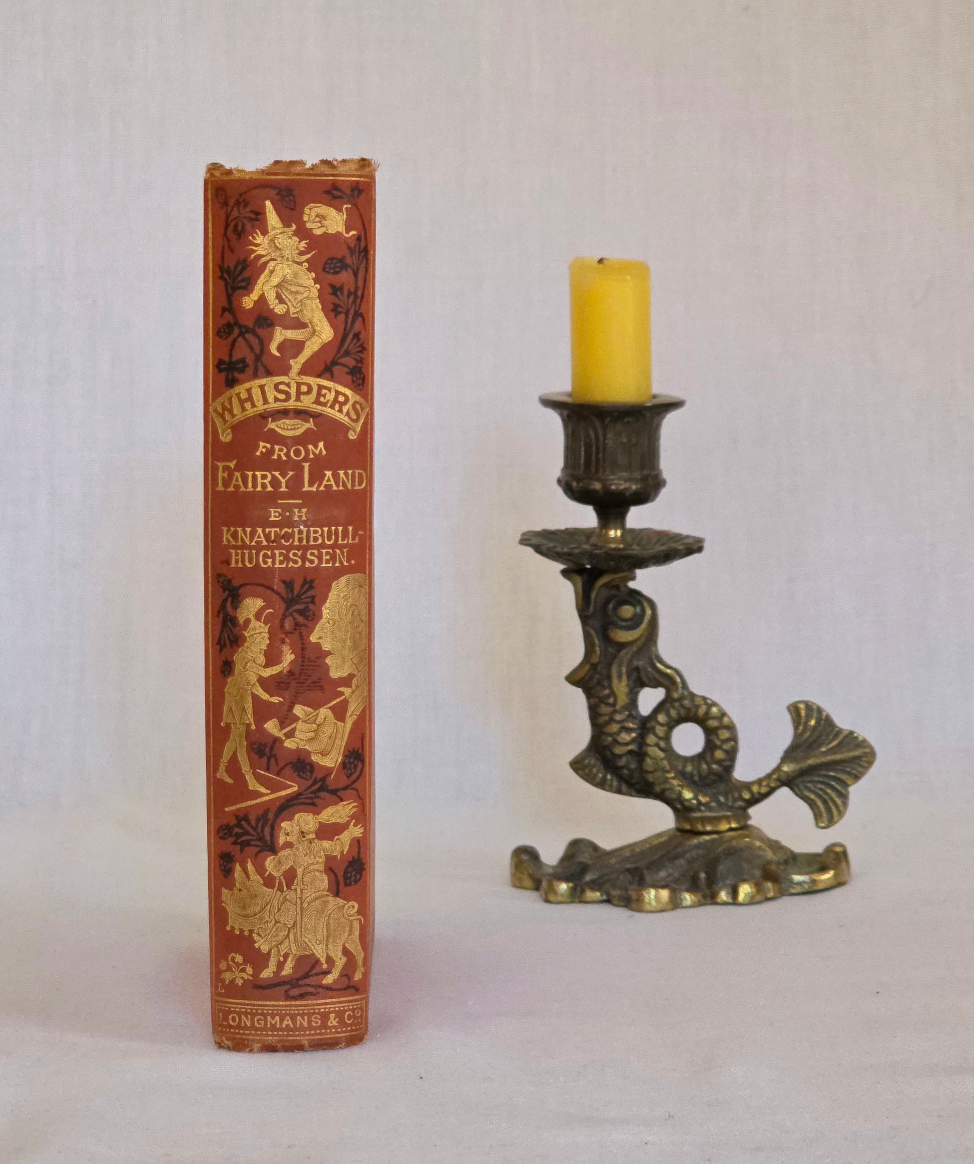 Antique book spine in red cloth with black and gold decoration saying 'Whispers in Fairyland' by Knatchbull-Hugesson